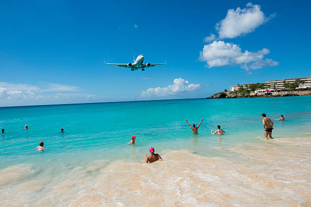 Maho Beach, St. Maarten - November 15, 2013: A commercial airliner descends over people enjoying a swim in the Caribbean Sea at Maho Beach. The plane is moments from touching down at Princess Juliana International Airport in St. Maarten.